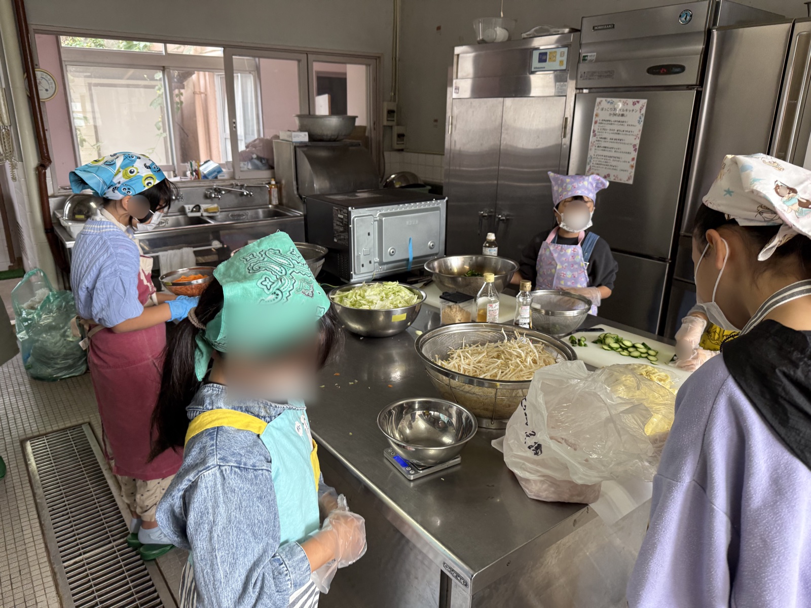 エプロンと三角巾をつけた子どもたちが、調理台を囲んで野菜の下ごしらえをする様子